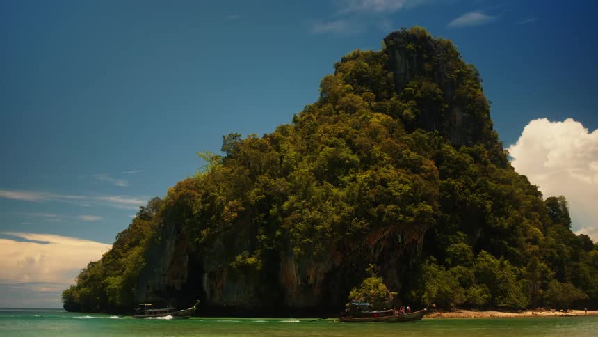 Boats pass by the shore of an island covered with a big mountain