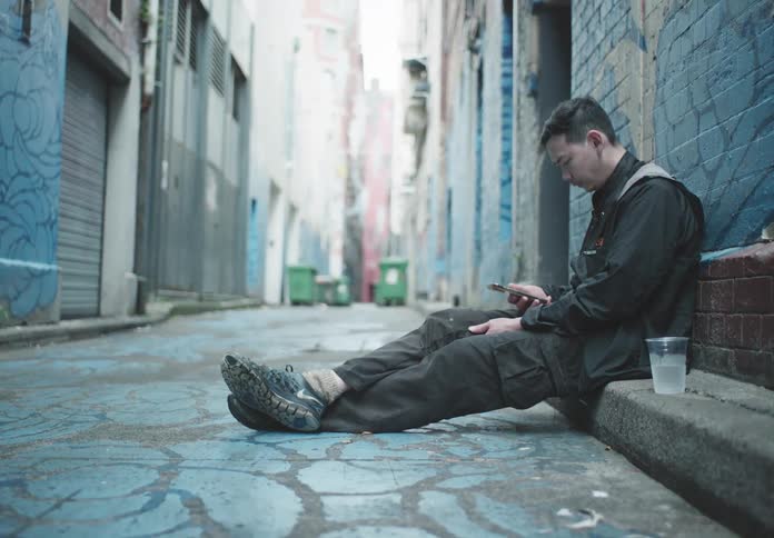 A man sits on the sidewalk on his phone