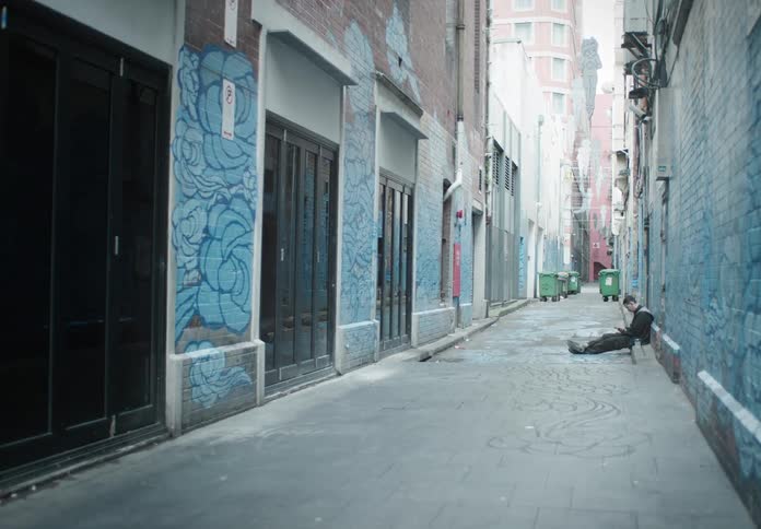 A man sits on the side of an alley