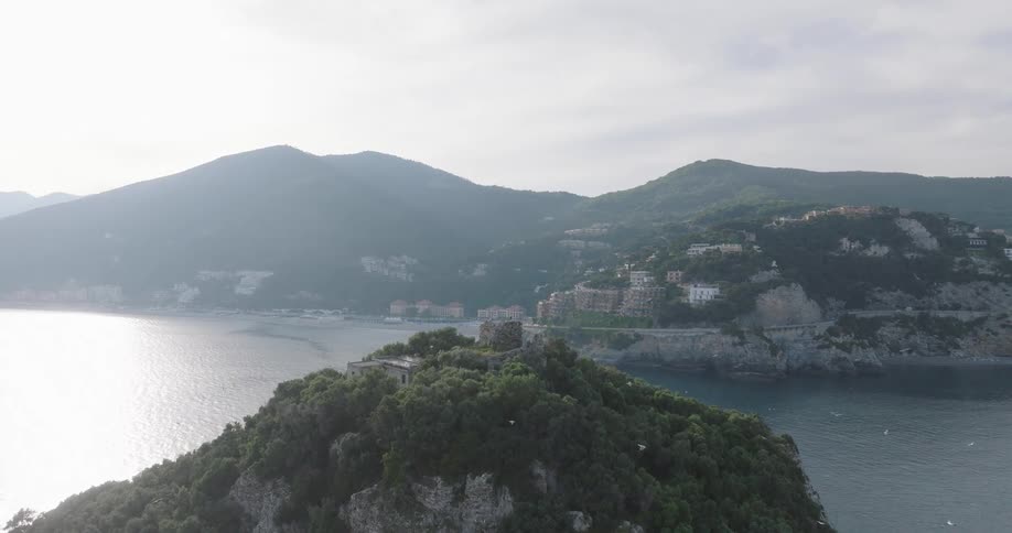 Aerial shot of an island surrounded by ocean and buildings and houses on wooded mountains in the background
