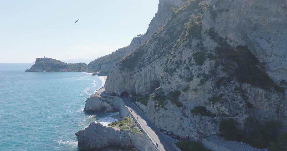 Aerial view of a highway between a turquoise beach and mountains