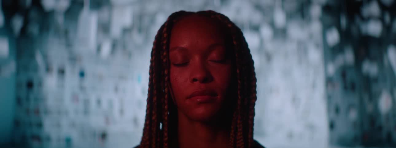 A young woman standing still staring straight ahead then slowly closing her eyes