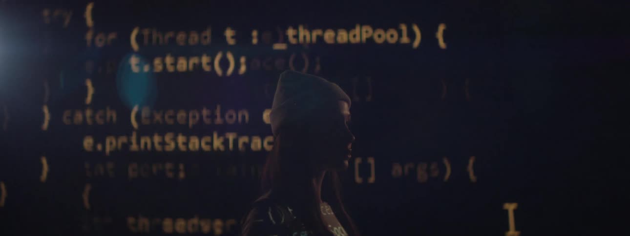 A woman wearing a beanie is silhouetted against a black screen displaying scrolling yellow computer code