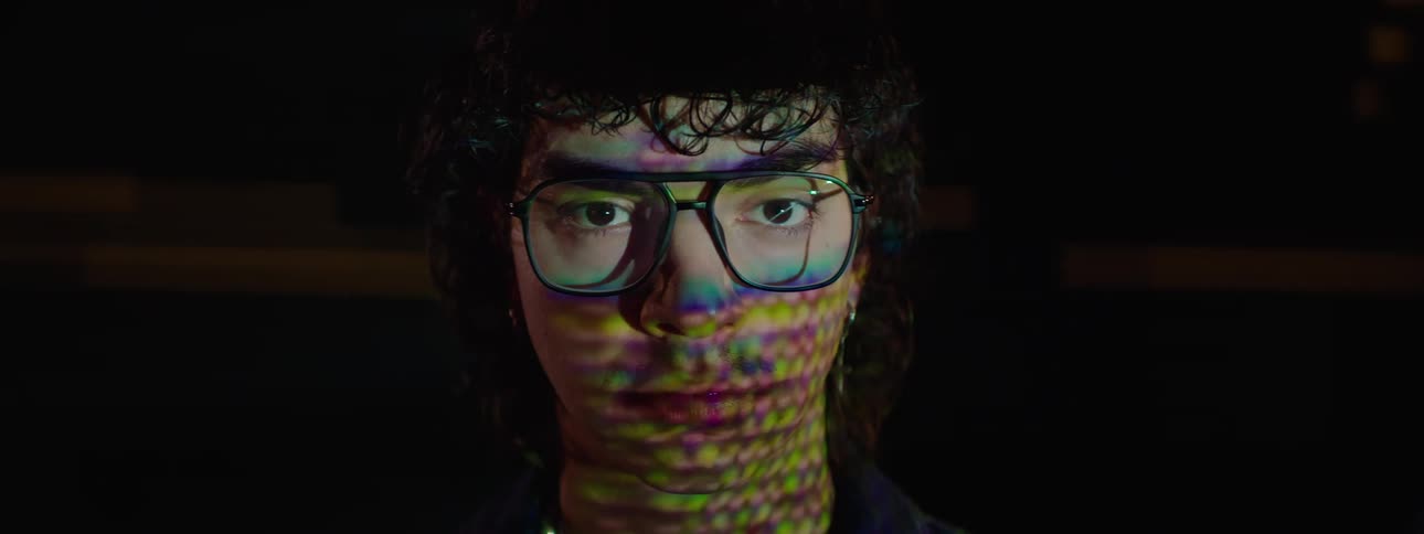 A man is sitting in front of a screen that reflects on his face