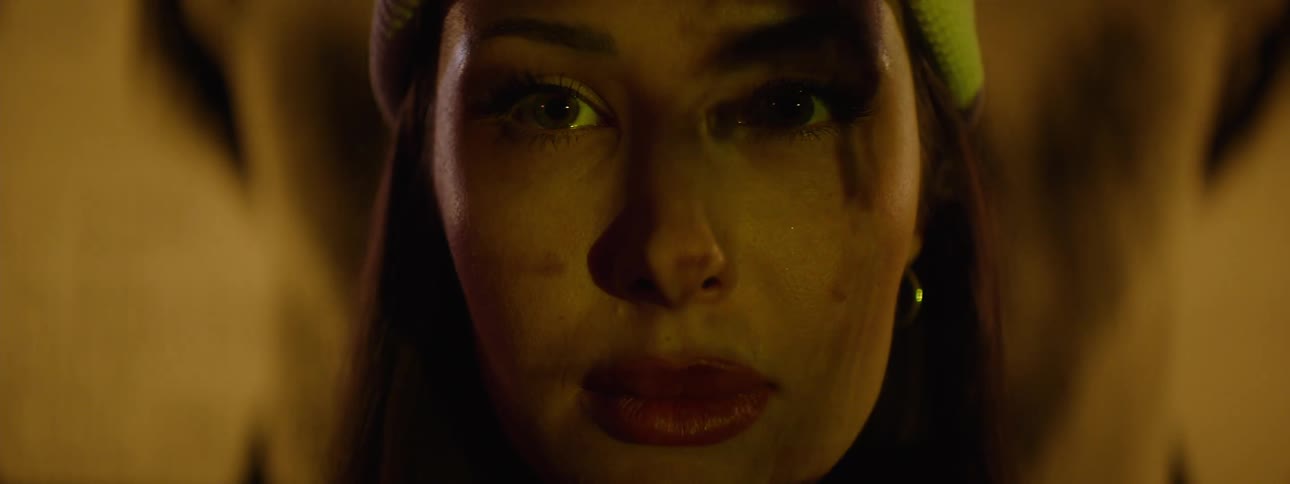 A woman stares intensely ahead in low dramatic lighting with shadows and a projected image crossing her face