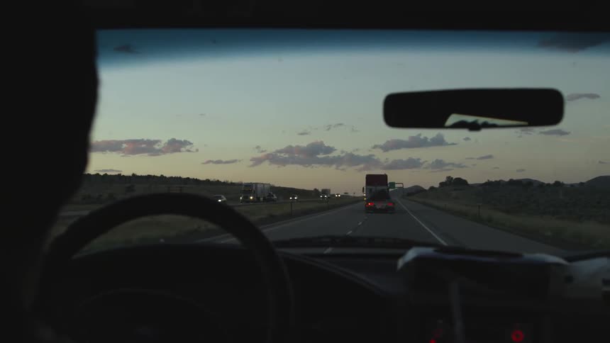 A person drives a car on the highway at sunset