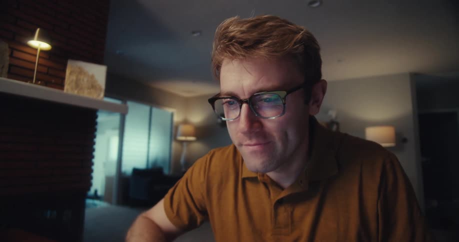 Man puts on his glasses and uses his computer after stopping and thinking while in his living room