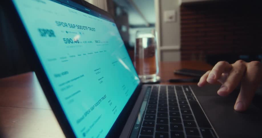 A focused man intently analyzes financial data on his laptop in a dimly lit home setting
