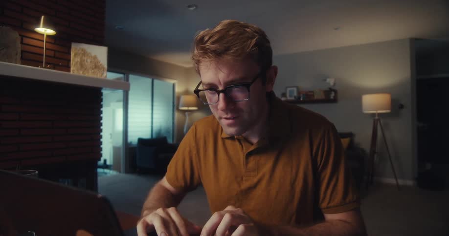 Man using a calculator and a computer while sitting in his living room smiles
