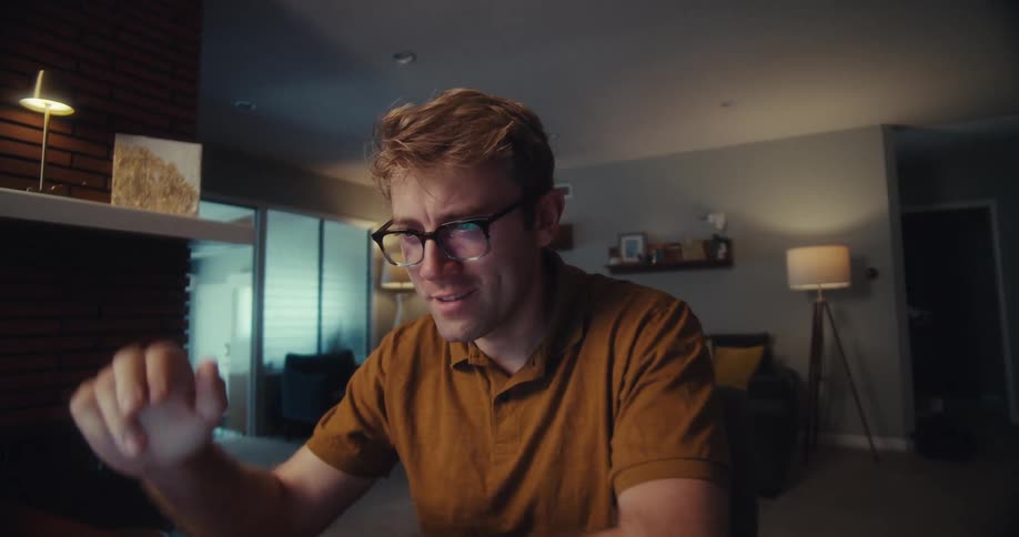 Man using a computer at home during the daytime smiles and takes off his glasses while thinking