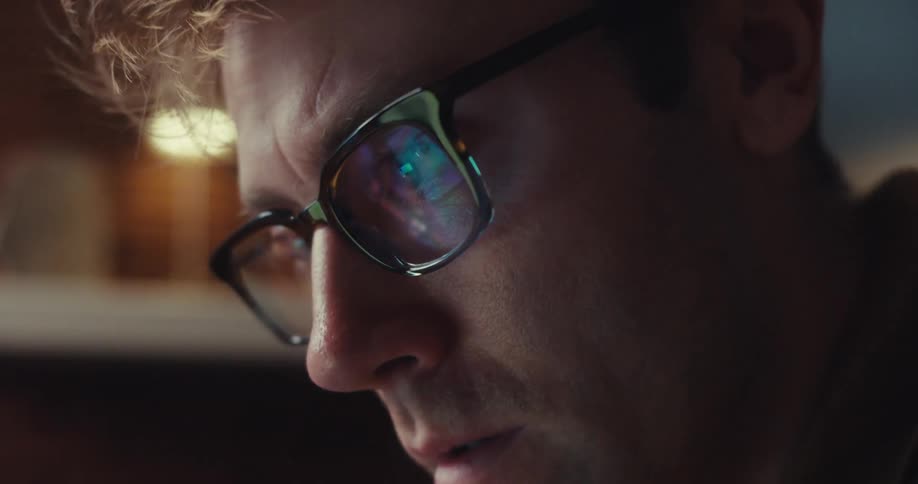 A man sitting behind a computer puts aside a calculator puts on his glasses and starts working on his computer while at home