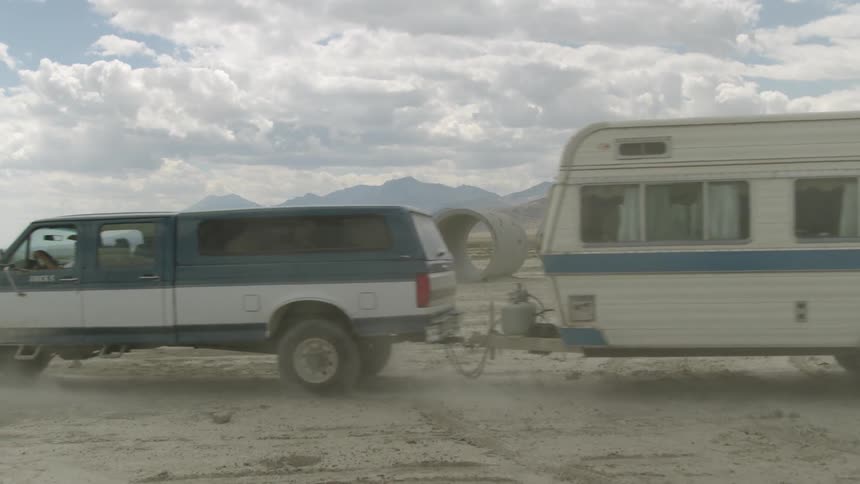 A truck pulling a camper drives through a dusty area