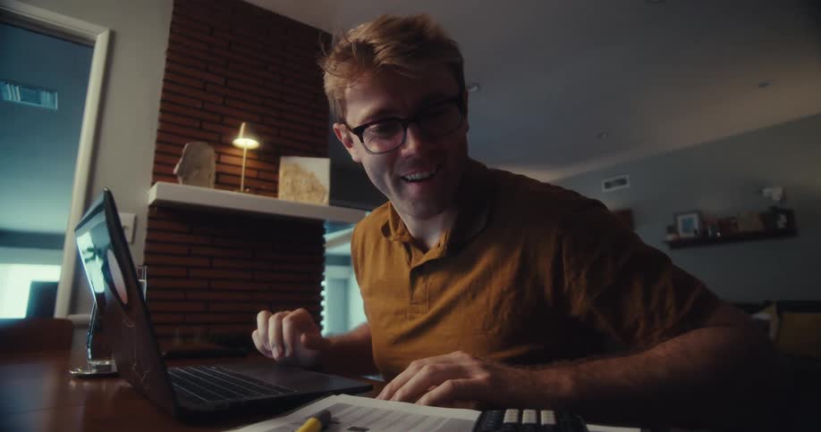Man working in front of a laptop and typing on a calculator next to him