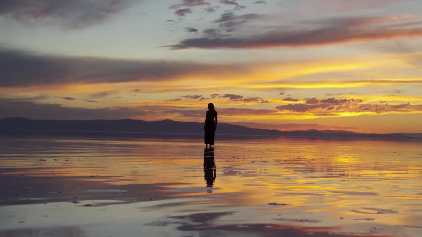 A woman stands on a shallow beach at dusk