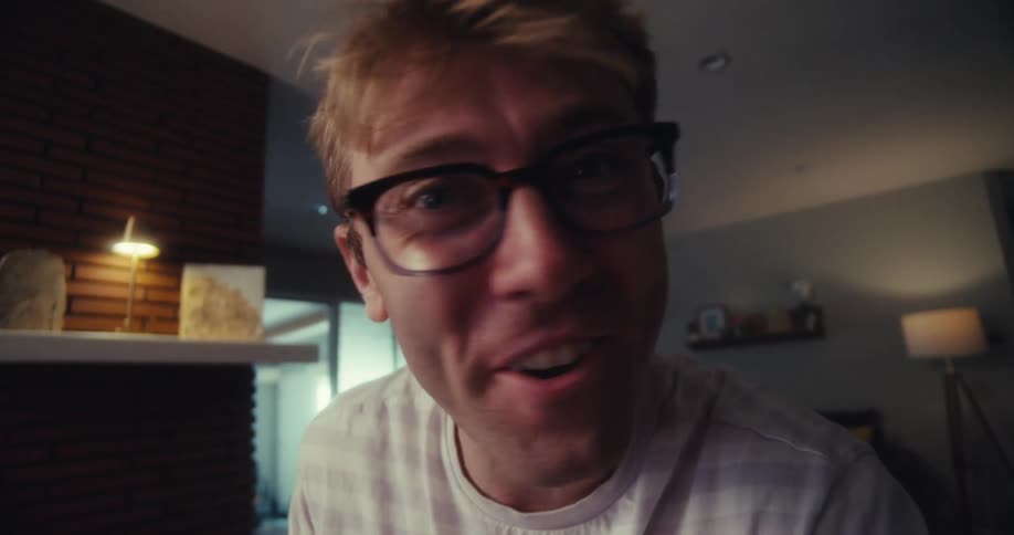 Man wearing eyeglasses while at home smiles and talks about a pair of sunglasses