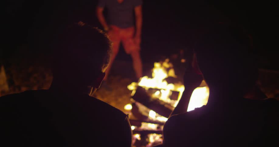 Campers sit around a burning campfire at night