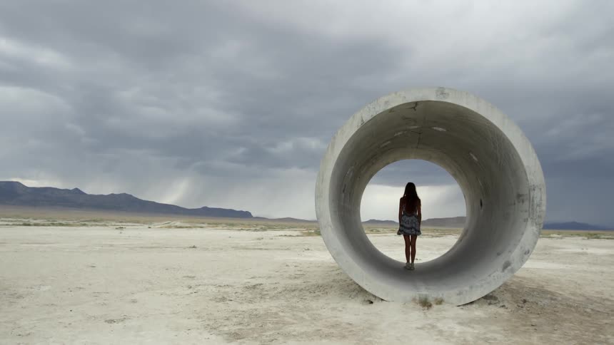 A woman is standing in a cylinder on the beach