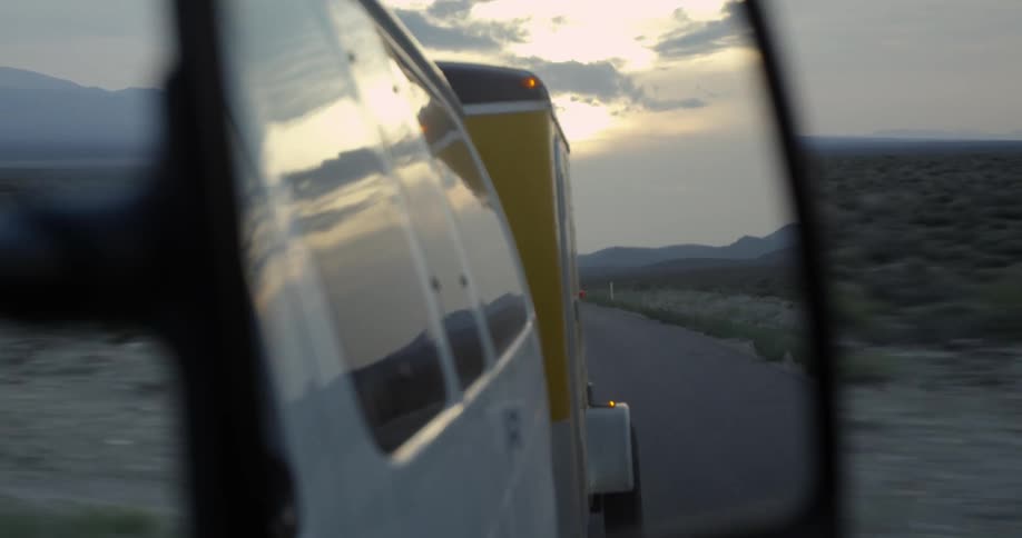 A van hauling a trailer drives down a desert road