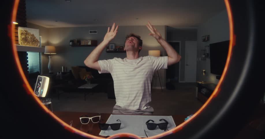 A man animatedly performs hand gestures while filming himself with a ring light in a stylish living room