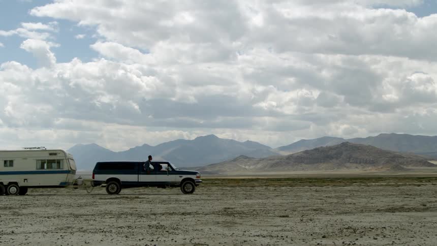A truck slowly driving across the desert pulling a trailer
