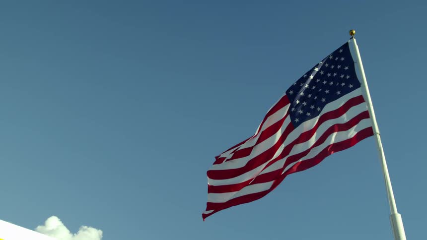An american flag blowing in the wind in front of a blue sky