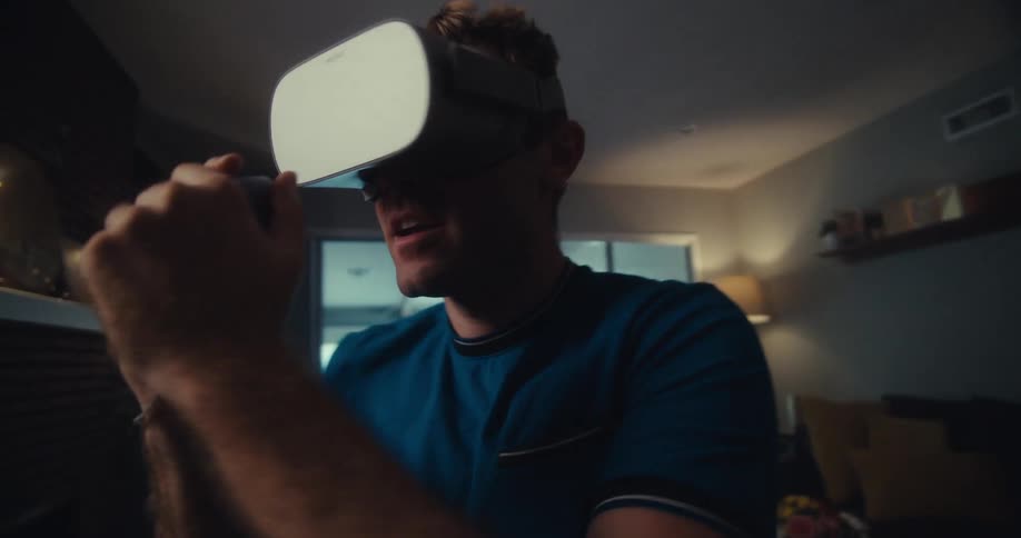 Man standing in living room wearing virtual reality glasses and holding a small gray controller