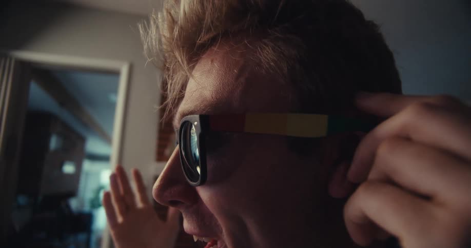 Man pushes back his hair while wearing sunglasses under video set lighting