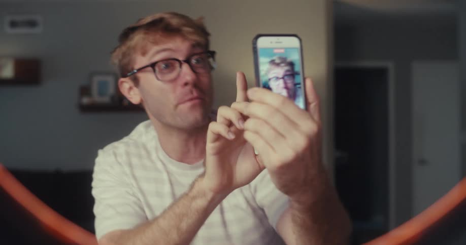A cheerful man excitedly shows off his sunglasses while recording himself on a smartphone