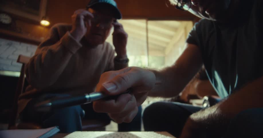 A man talks with a friend and points to something with his pen