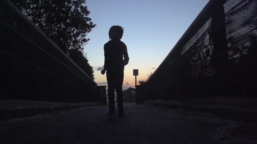 Small child running down a paved path and sunset