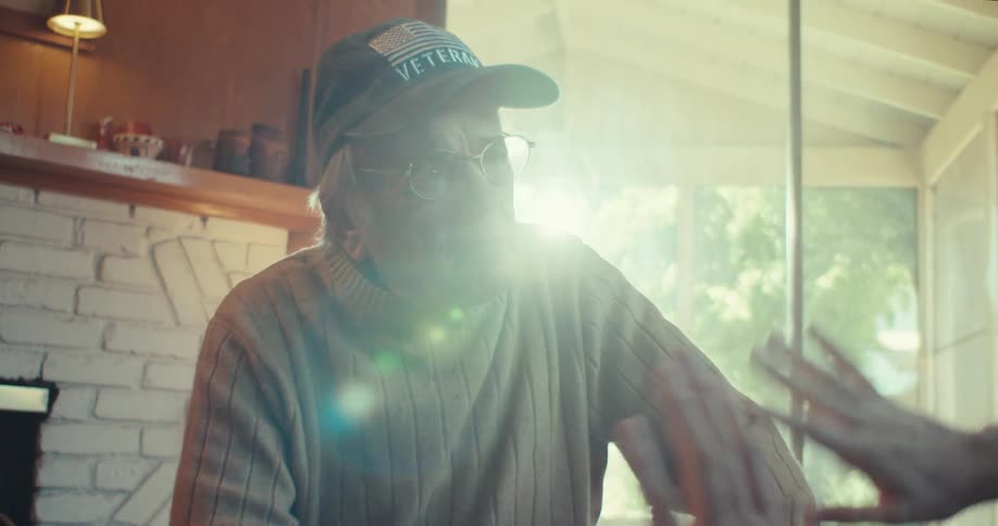 An elderly man listens attentively to another man explaining something with a laptop open on a coffee table in front of them at midday