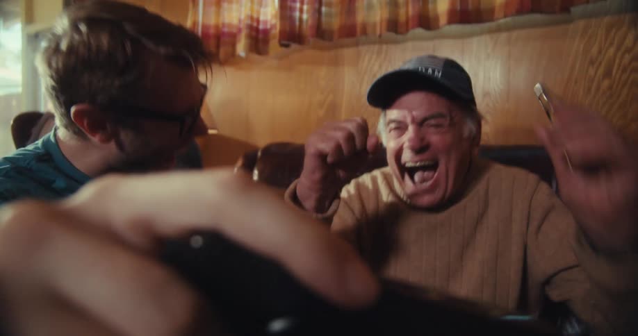 Elderly man and another man happily celebrating together while watching something on a smartphone