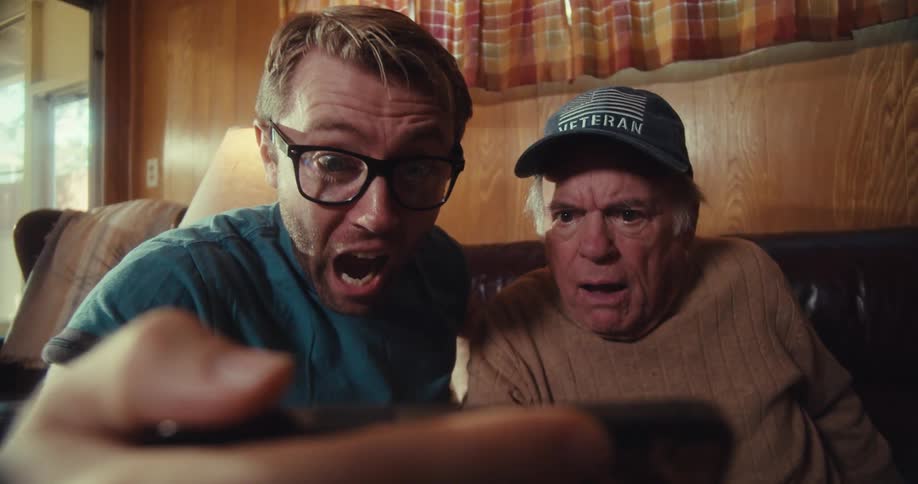 Young man sitting holding smartphone and watching something together with elderly man and both cheering happily together