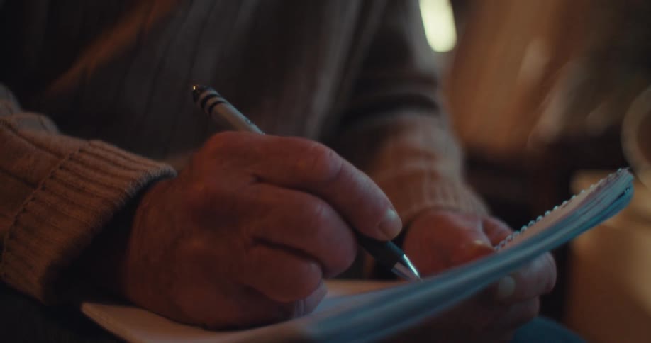 Person accompanying an elderly man writing in a notebook