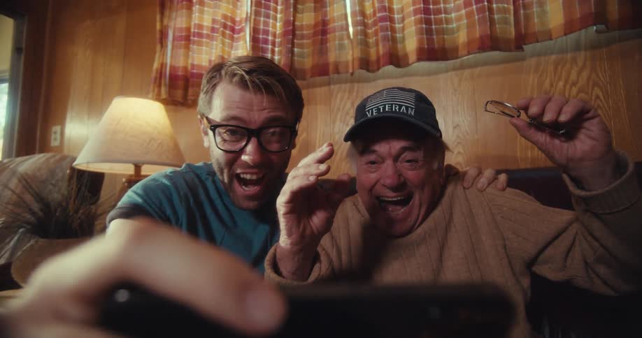 Elderly man and a man watching together on a smartphone and cheering happily