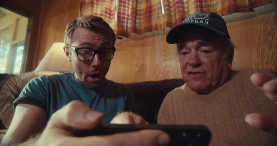 Two men sitting on the couch cheer at a cell phone