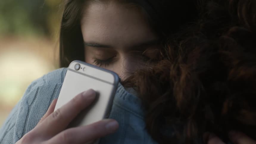 A woman hugging someone with a phone in her hand