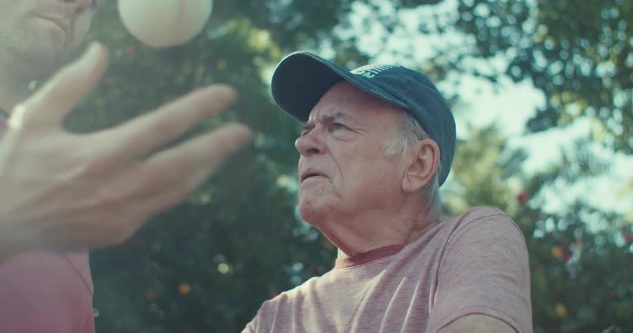 Man holding a baseball with an elderly gentleman by his side