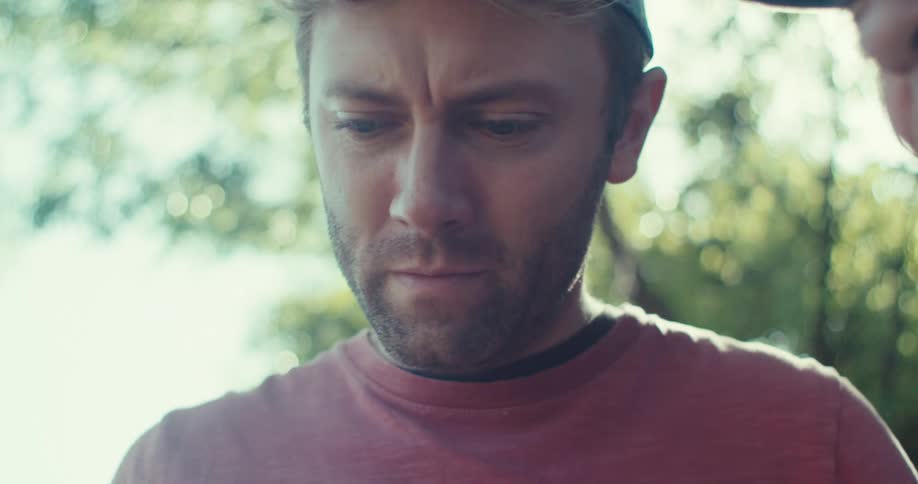 Two men observe something carefully under the bright sunlight in a wooded environment