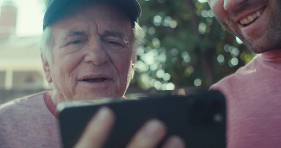 Two men are looking at a cell phone outside