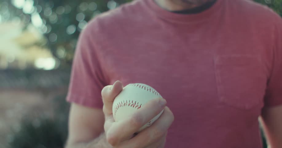 A man holds a baseball while standing outdoor in the morning