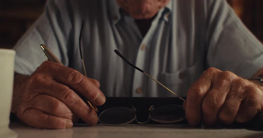 Man holds a pen and his glasses on the table