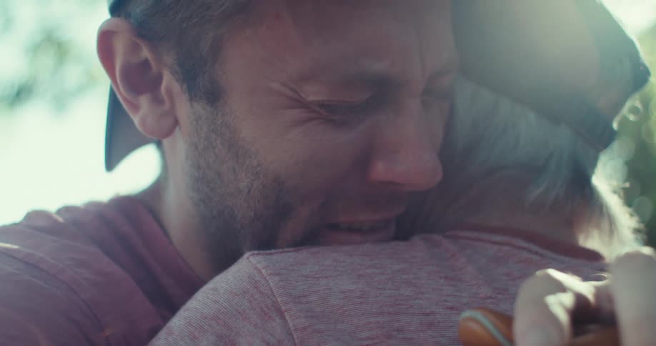 Young man hugging an older man and showing an emotional response under bright sunlight
