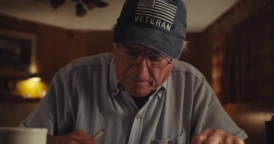 Elderly man in cap sitting at a table interacting with tablet