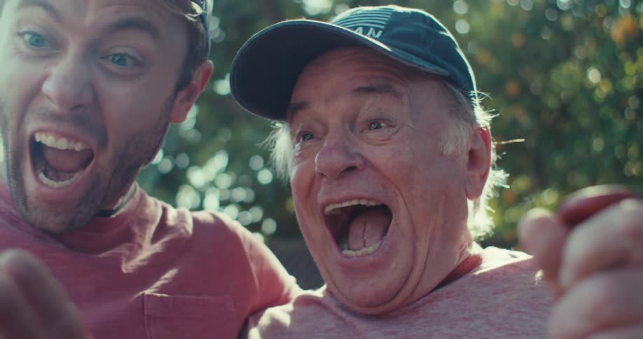 Two men look at a cellphone and laugh as they stand outside