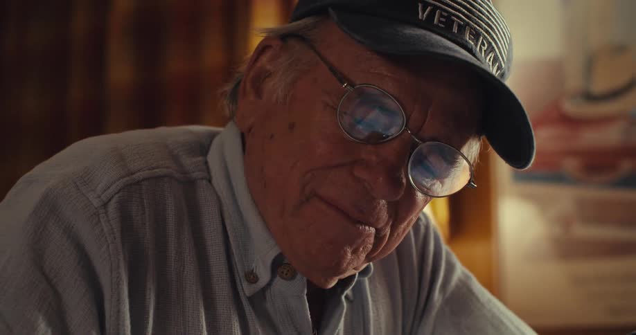 Elderly man in cap and glasses writing