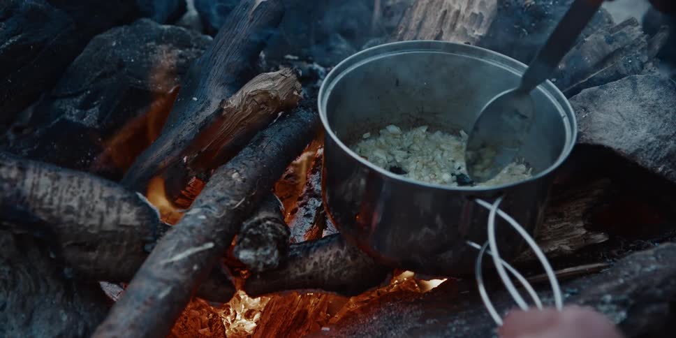 A man cooking onions in a pot over a campfire