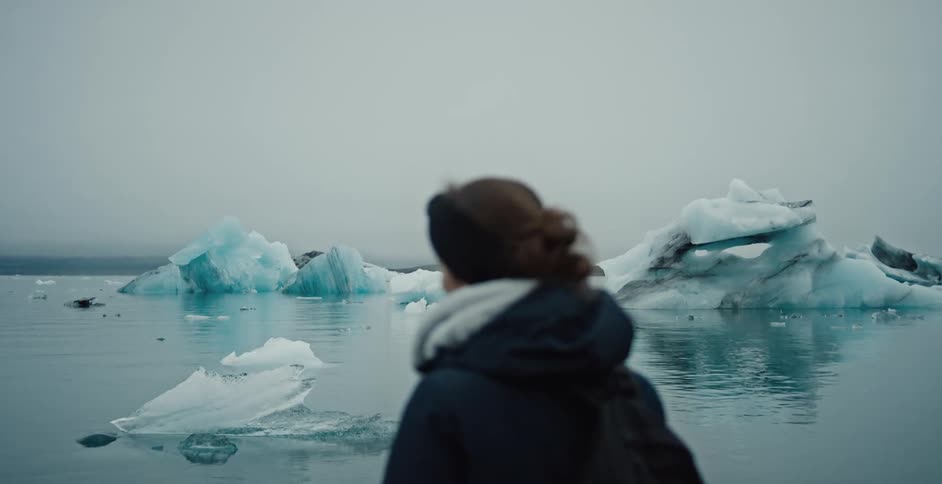 Woman watches ice floes floating on a glacial lagoon under a gray sky and freezing atmosphere