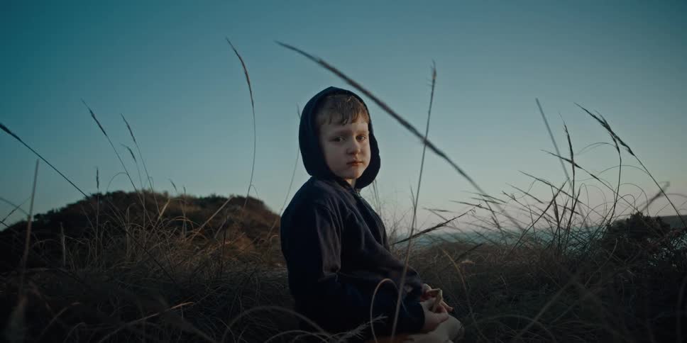 A kid sits in the reeds and chews his food