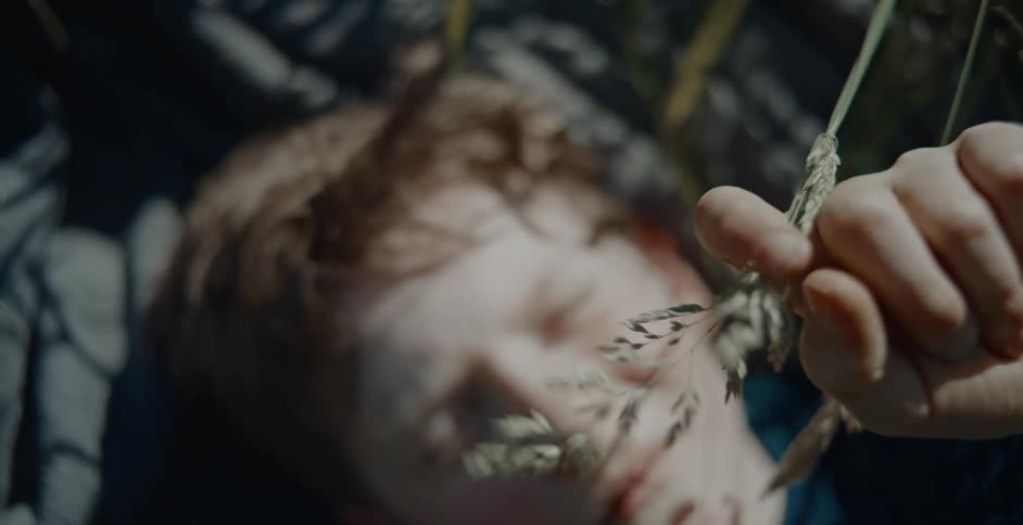 A young boy lies on the floor playfully moving a blade of grass with his finger